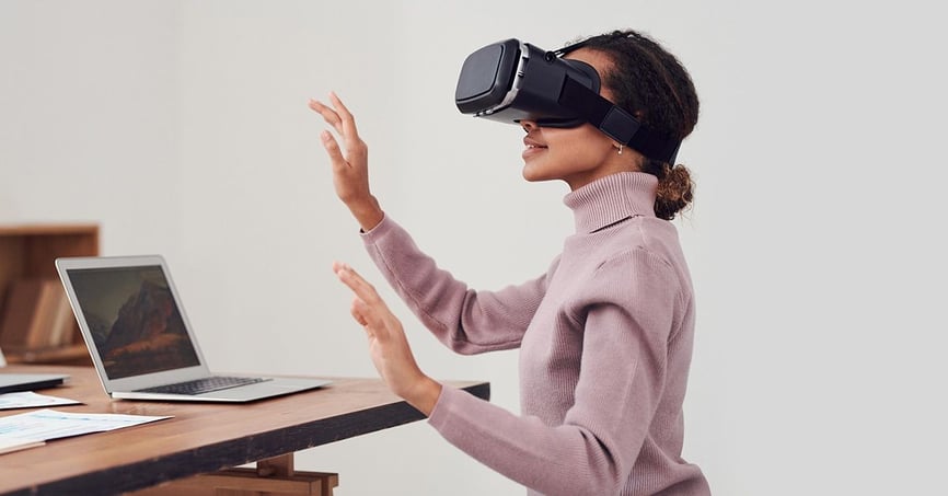Eine Frau benutzt ein VR-Headset auf ihrem Schreibtisch, auf dem sich Notizen und ein Laptop befinden