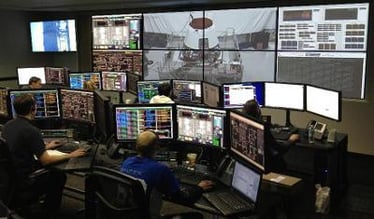 Ein Kontrollraum mit Mitarbeitern an ihren Arbeitsplätzen und einer Videowand, die Live-Bilder und Daten anzeigt