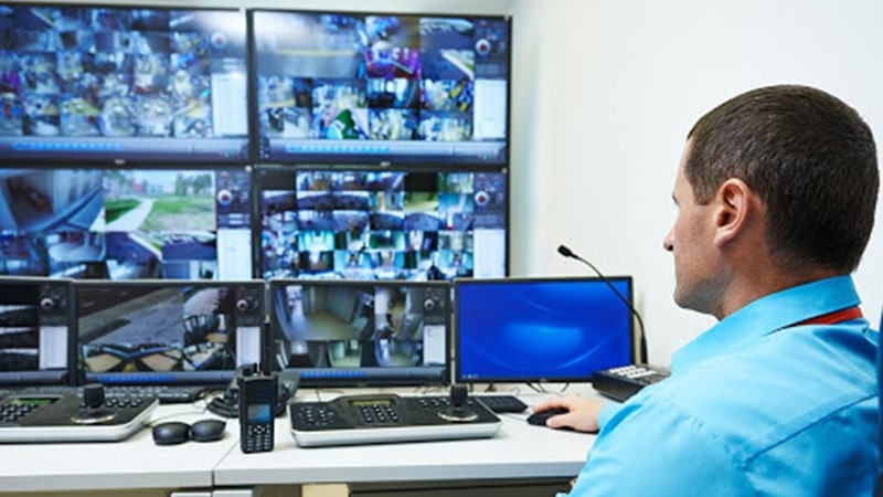 Mann in der Sicherheitszentrale des Campus, der den Campus über eine Videowand mit Live-Kamerabildern überwacht