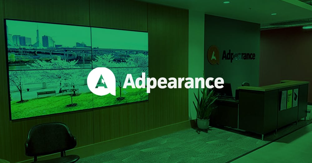 Leeres Foyer von Adpearance, mit einer von Userful betriebenen Videowand, die hinter einer Sitzecke Fotos zeigt, und einem Empfangstresen mit dem Adpearance-Logo an der Wand dahinter mit grünem Overlay und Logo