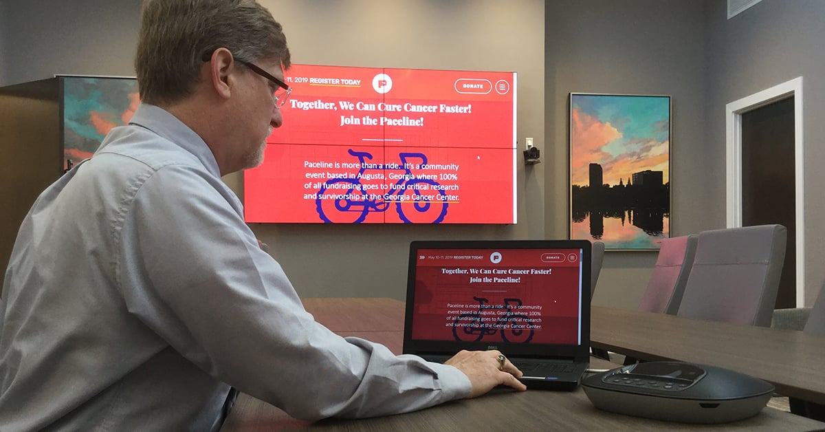 Besprechungsraum des Medical College of Georgia, in dem ein Mann mit seinem Laptop und Userful eine Webseite auf einer Videowand hinter ihm anzeigt