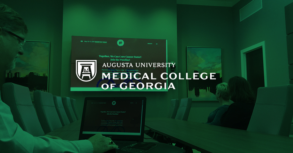 Besprechungsraum des Medical College of Georgia, in dem ein Mann mit seinem Laptop und Userful eine Webseite auf einer Videowand hinter ihm mit grünem Overlay und Logo anzeigt