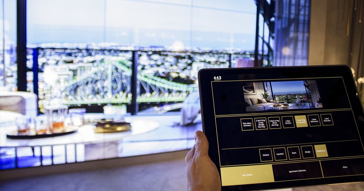 Q1 Design-Verkaufsbüro in Australien mit einer Videowand, auf der Fotos von Immobilien gezeigt werden, die über eine Tablet-Schnittstelle ausgewählt werden