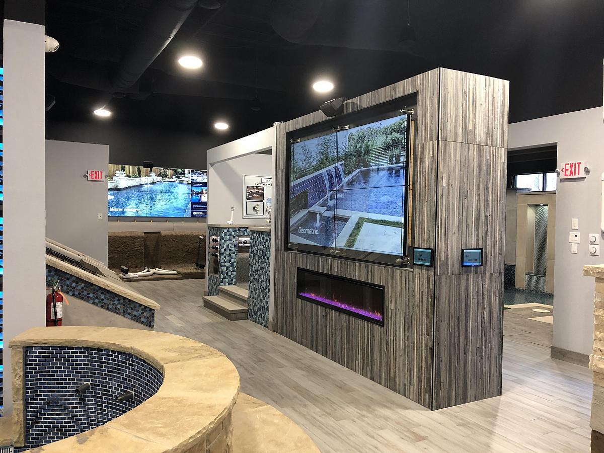 Pool-Showroom mit modernem, freistehendem Kamin mit eingebauter Videowand, die Poolwerbung zeigt