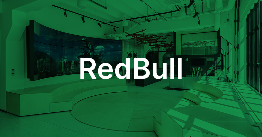Lobby der Redbull-Zentrale in Polen, mit treppenförmigem Sitzbereich, Rezeption und einer gebogenen Videowand, auf der ein Red Bull-Werbespot mit grünem Overlay und Logo gezeigt wird