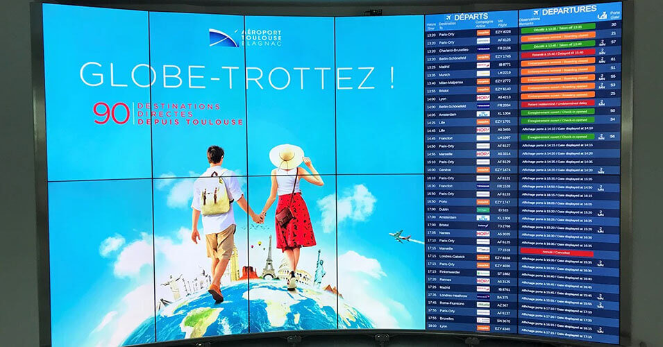 Video wall in Toulouse-Blagnac Airport displaying advertisement and departure times for flights